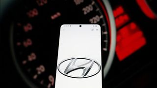 A phone screen displaying the Hyundai logo, with a car's dashboard in the background