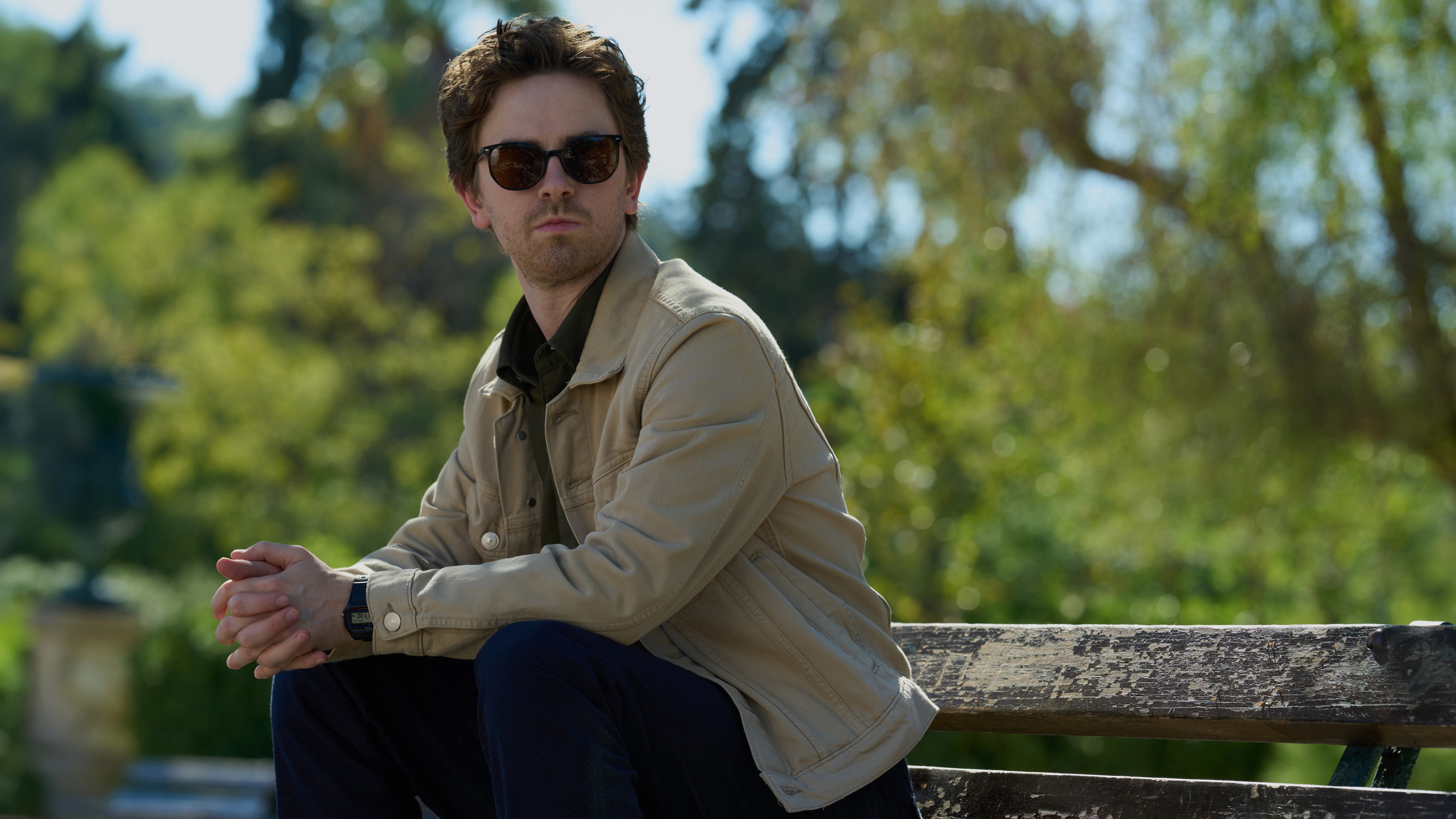 Edward sitting in a park wearing sunglasses while waiting for Jasper.