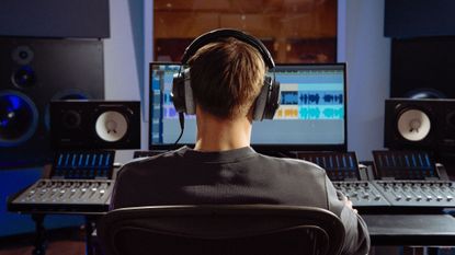 A man sits at a mixing desk listening to his creation on a pair of Beyerdynamic DT-990 Pro X headphones