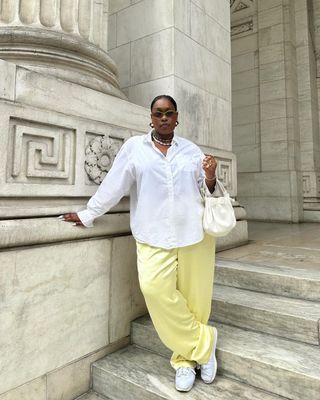 @aniyahmorinia posing on steps wearing white button down, yellow satin trousers, and white sneakers