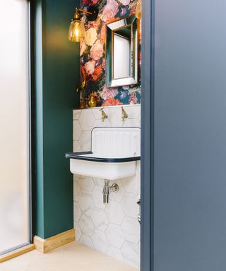 A bathroom idea situated in downstairs cloakroom with floral printed wallpaper, green and blue painted wall decor, white sink and white tiling