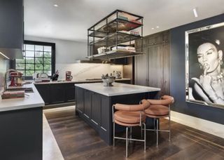 kitchen island with suspended shelves above and dark wooden floors. The kitchen island also has two peach colored bar stools.