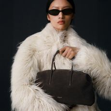A model wearing a fluffy white coat and holding a brown handbag from DeMellier.