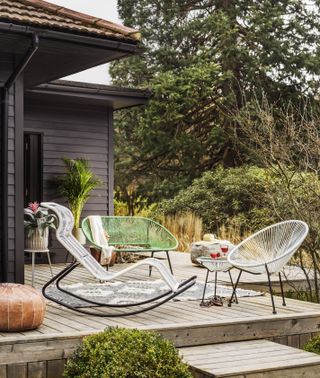 An outdoor space with decking and assortment of outdoor seating including white wire rocking chair decor