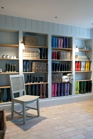 A mudroom with floor to ceiling storage for wellies and wicker baskets behind a chair