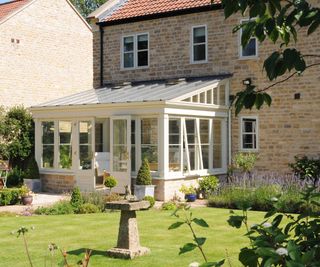 lean to cream conservatory with solid roof on rear of stone faced house