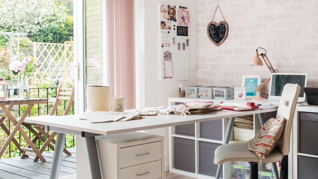 A garden office with a veranda with seating outside and a large desk inside with storage drawers