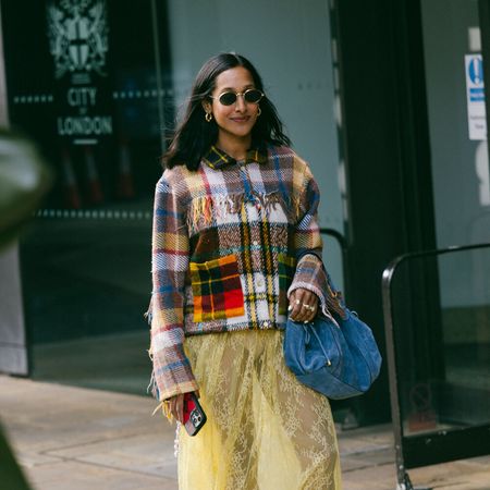 Woman wears plaid jacket, denim handbag, yellow sheer lace skirt, and mesh flats. 