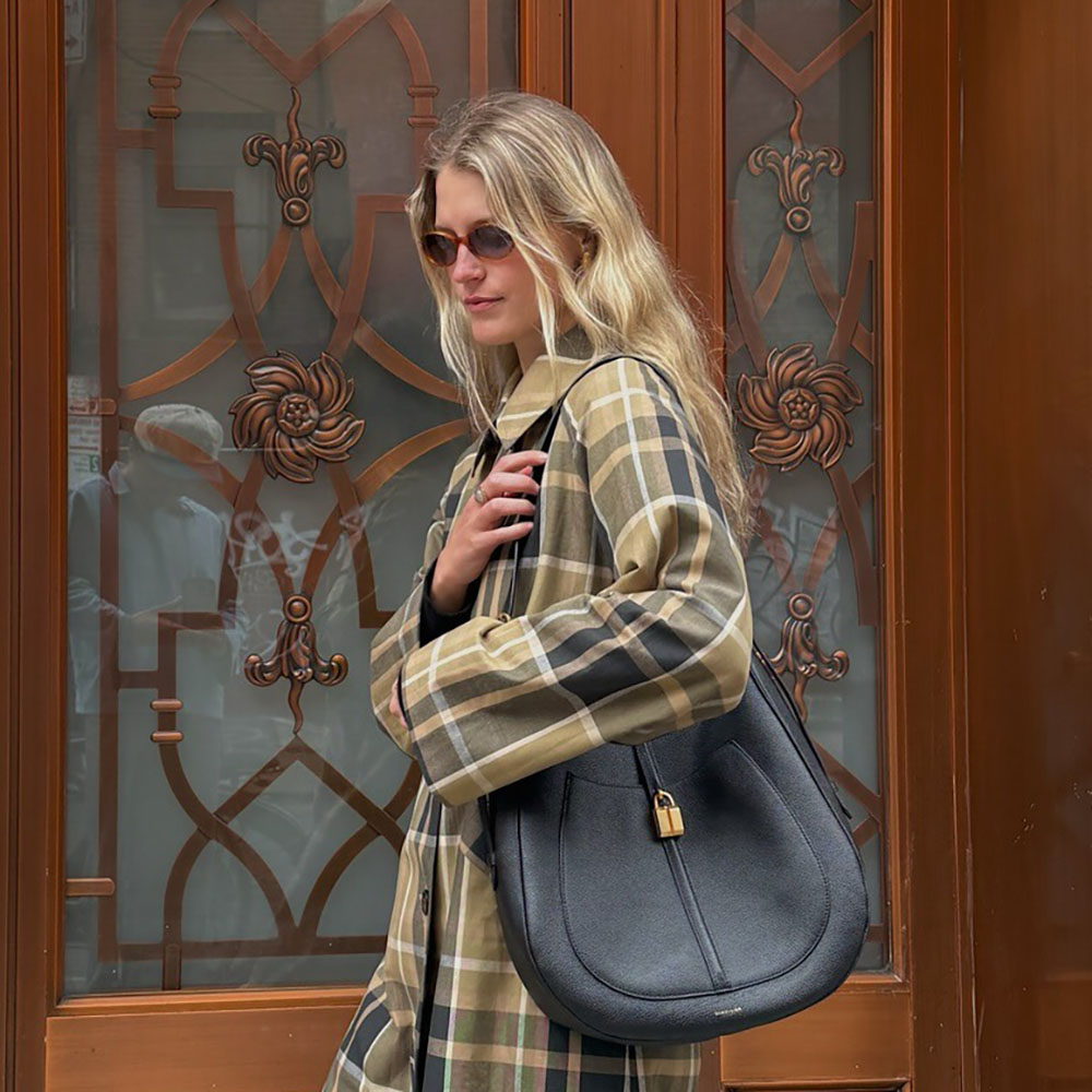 a woman wearing a plaid jacket and black leather bag