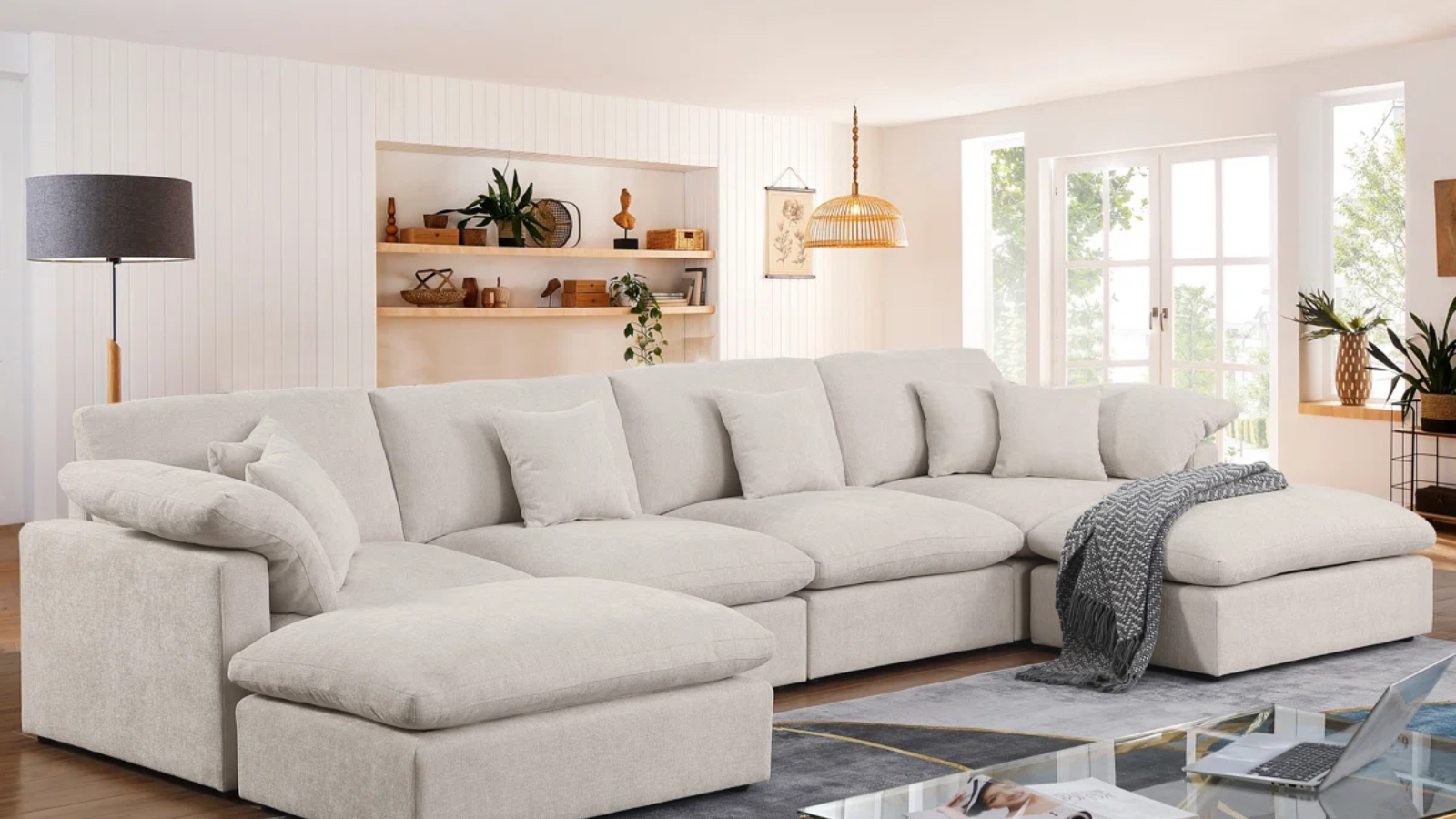 a living room with a large cream sectional, a lamp, and a blanket draped over the couch