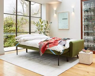 A green velvet sofa bed in a high-ceilinged apartment