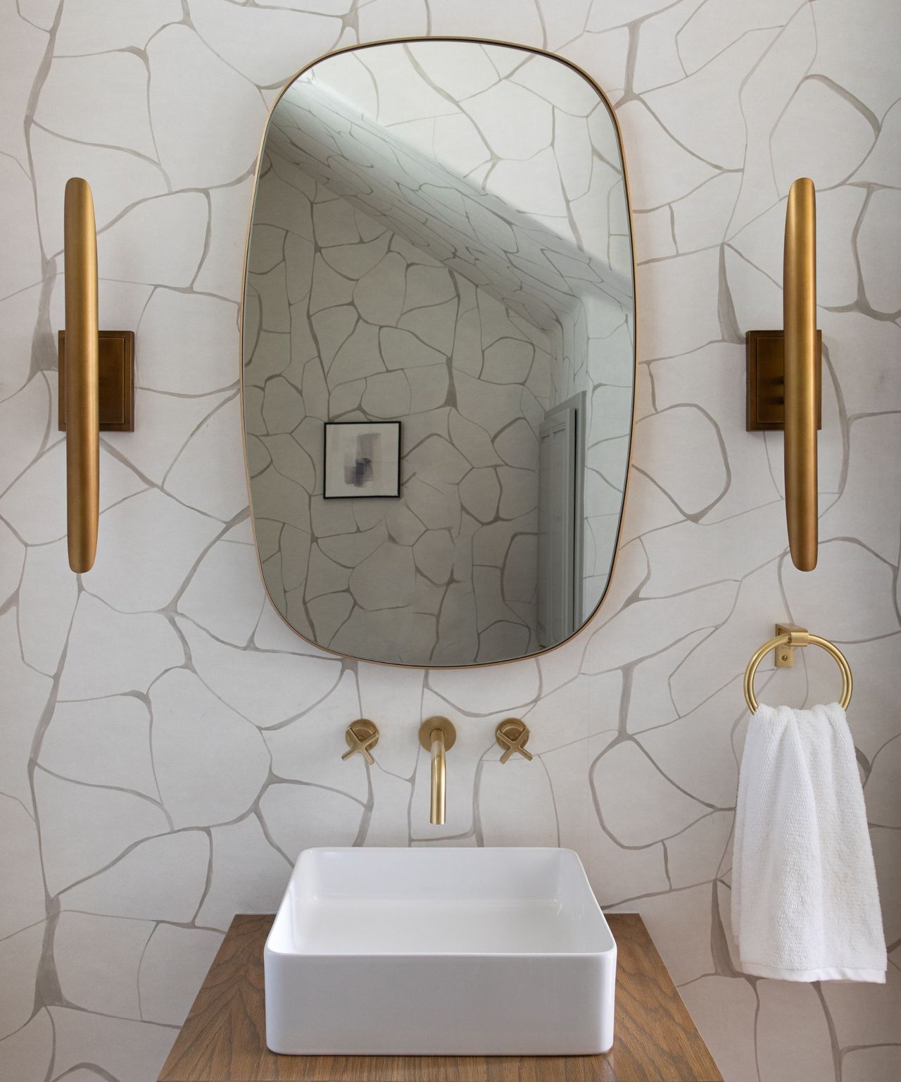 A powder room with a gold mirror and two matching sconces