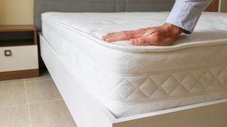 A man presses his hand on a mattress to check its support