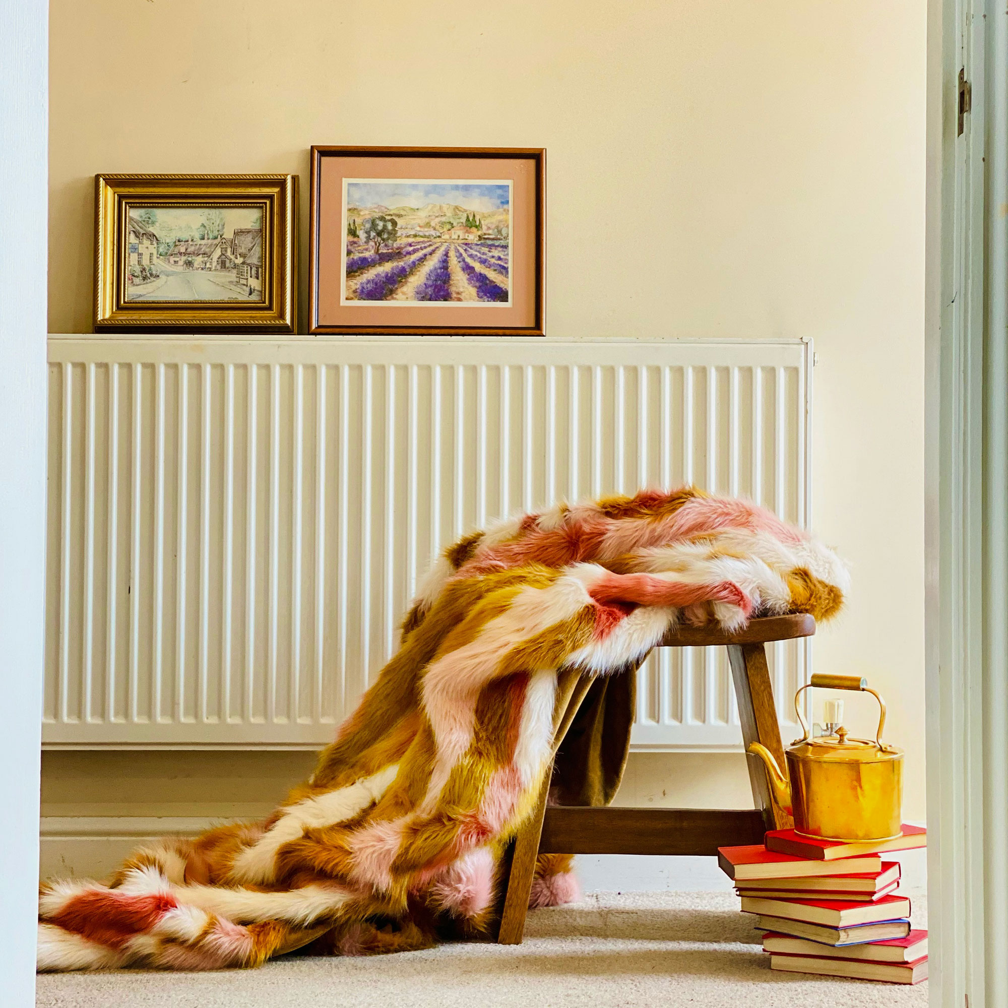 Neutral hallway with colourful faux fur throw on top of wooden stool
