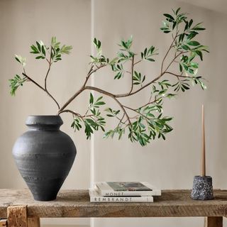 A circular black vase with a large faux olive branch