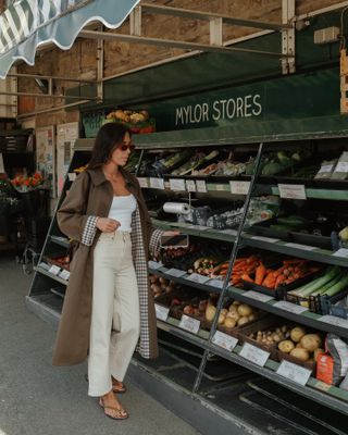 Ein Influencer trug eine lange Jacke, beige Jeans, beige Flip-Flops, ein weißes Tanktop und eine rote Sonnenbrille.