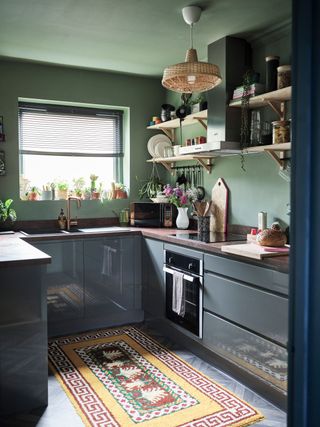 Aluminum Venetian blind in green painted kitchen with gray cabinets, wooden countertops, tribal rug and rattan decorative accents