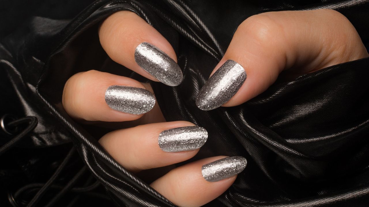 a woman&#039;s hand with silver glitter nail polish on her fingernails