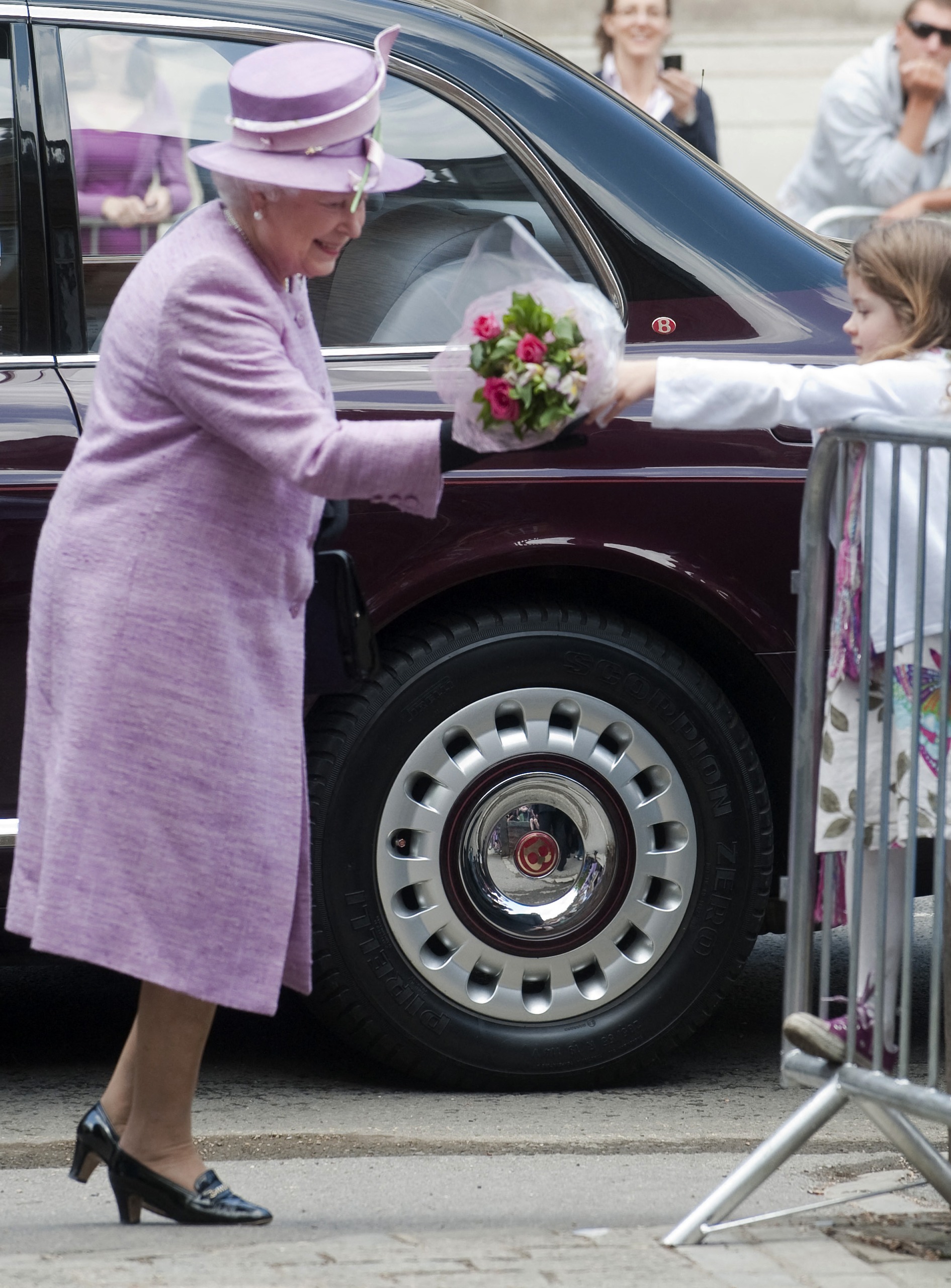 Queen Elizabeth wears a lilac coat and matching hat with a green feather and drops a bouquet given to her by a royal fan in 2010 at Eton