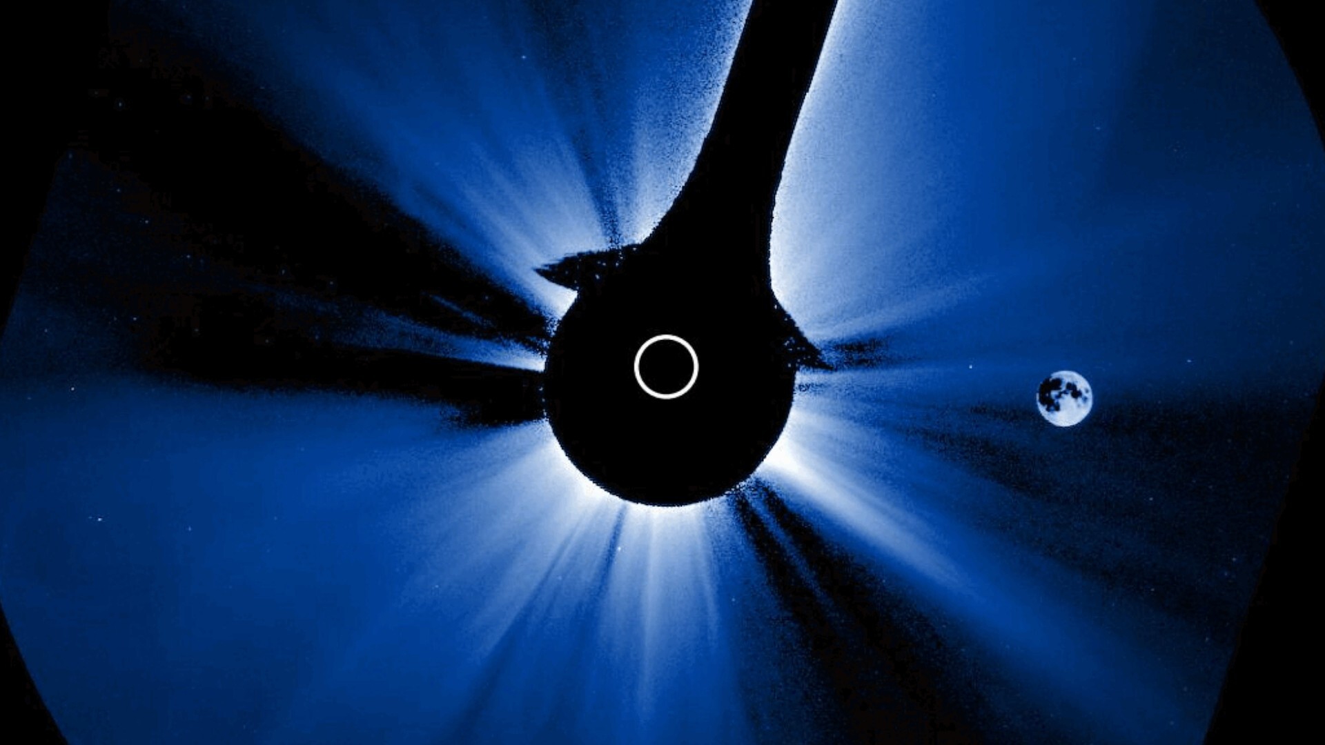 A black circle has a ring of white in it as it covers the center of the image, with blue and white light streaking out from the middle of the photograph
