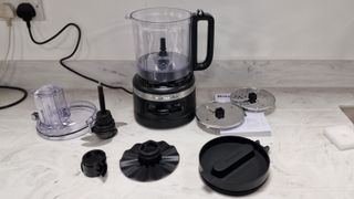 KitchenAid 9-Cup Food Processor with all its attachments on a white marble countertop