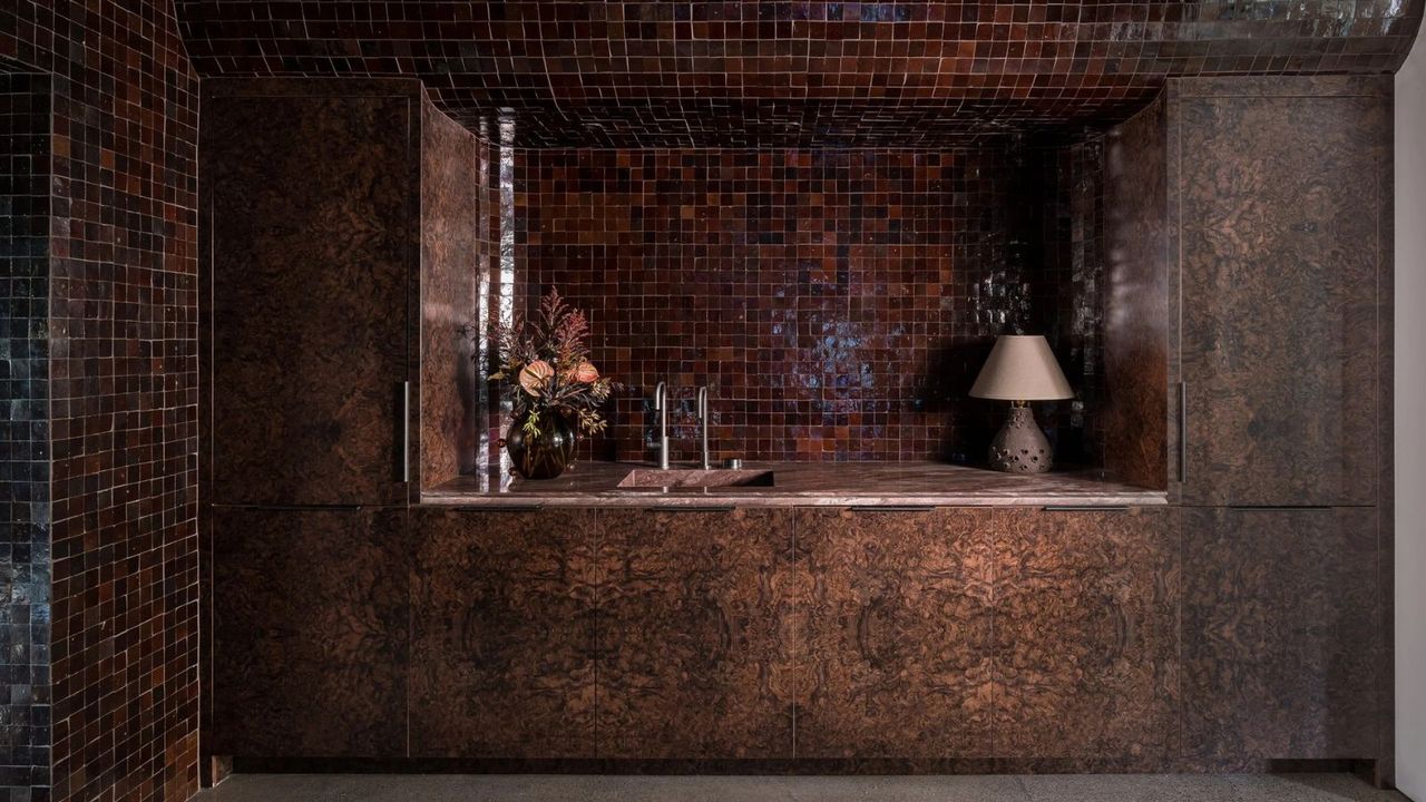 a bar area with burl wood cabinetry, dark brown zellige tile, a sink, and a vase of flowers on the countertop