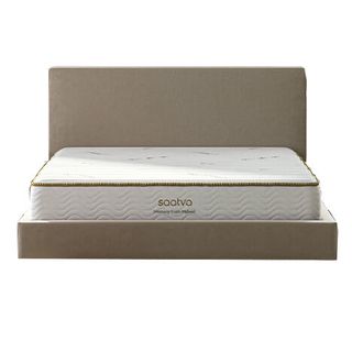 Image shows the Saatva Memory Foam Hybrid on a beige fabric bed base