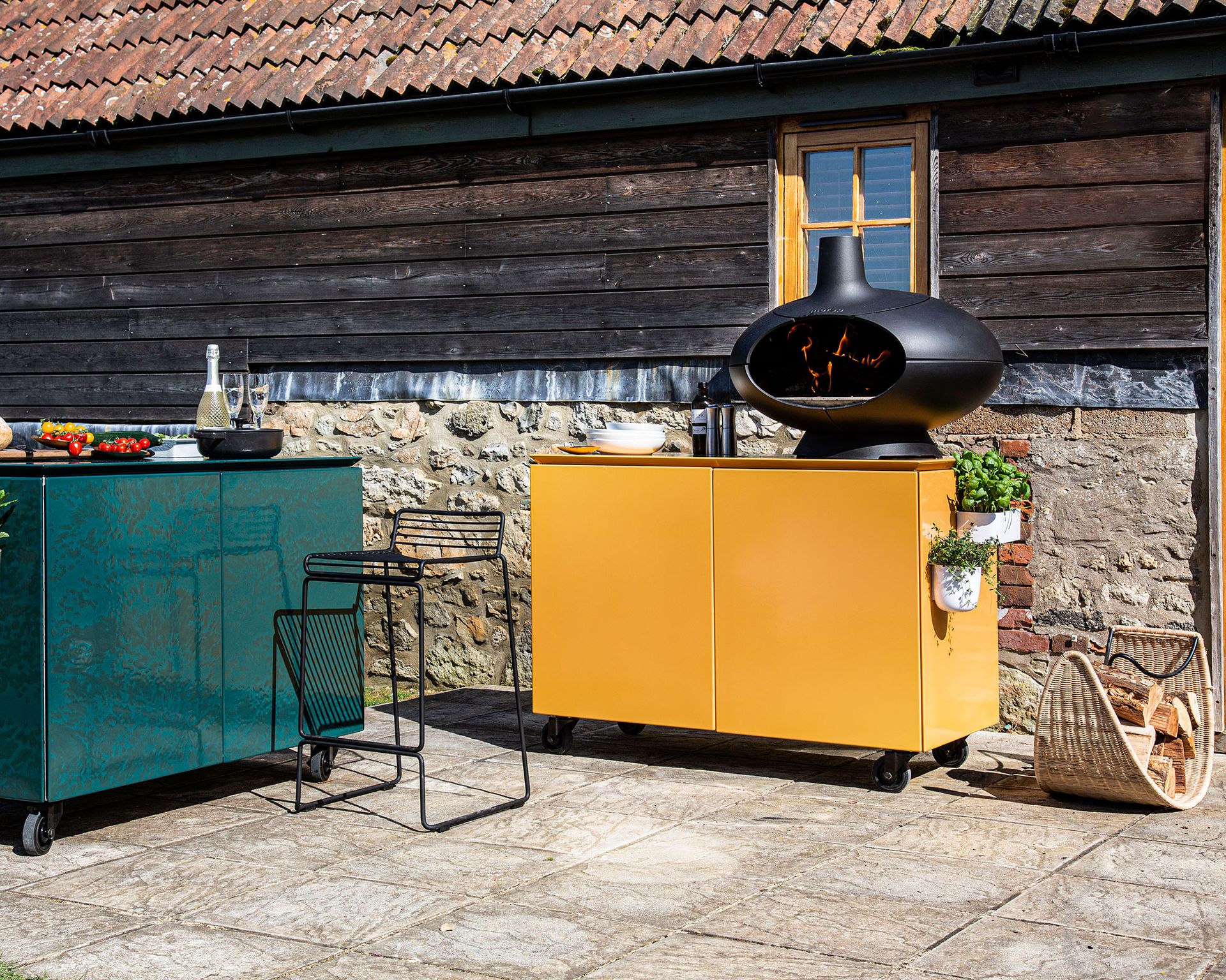 An outdoor kitchen with a yellow unit and a black pizza oven in a backyard patio