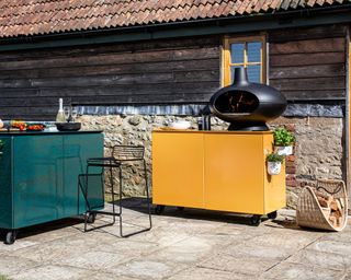 An outdoor kitchen with a yellow unit and a black pizza oven in a backyard patio