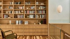A wood bookshelf wall with colorful books, lamps, ceramics, and a pendant lamp. Also pictured is a green woven chair.