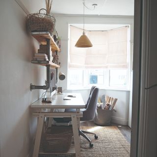 A small home office with a desk against the wall and storage baskets on the bottom and industrial-style shelves above it