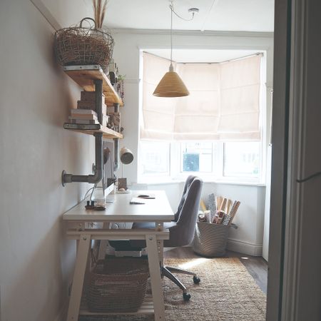 A small home office with a desk against the wall and storage baskets on the bottom and industrial-style shelves above it