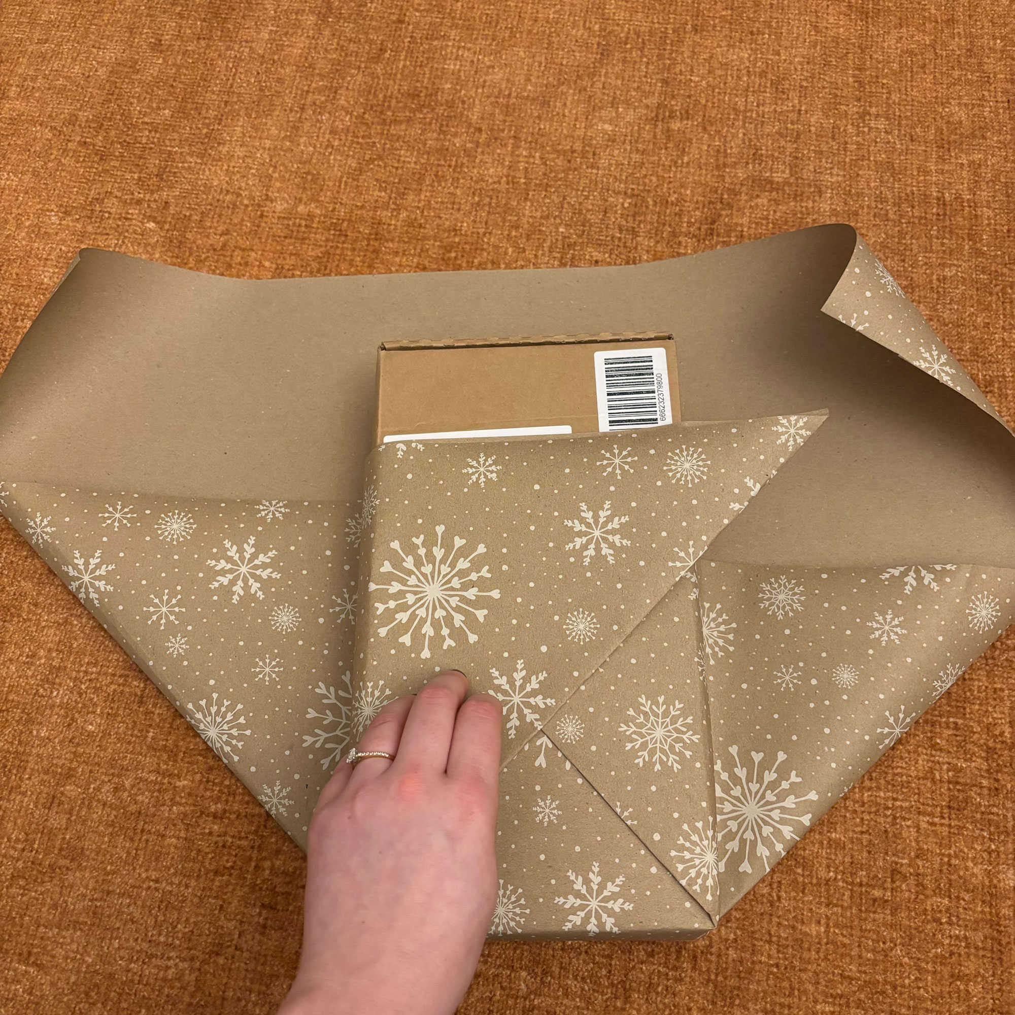 A rectangular box wrapped in brown paper with a white snowflake print on it