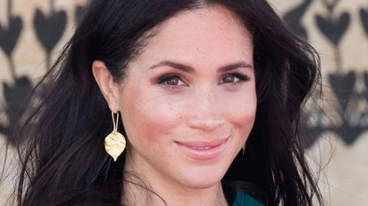 Meghan Markle looking at the camera in gold earrings and a teal dress