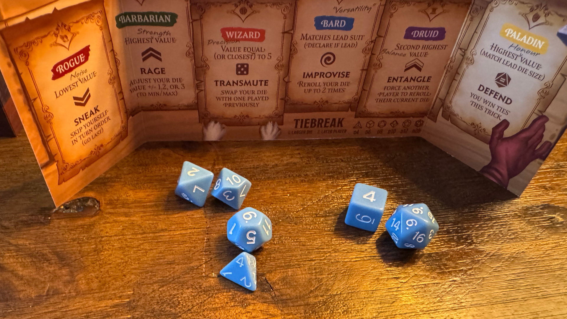 A series of blue dice in front of a player screen, all on a wooden table