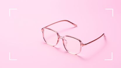 Pair of transparent reading glasses on light pink background to symbolise eyesight getting worse