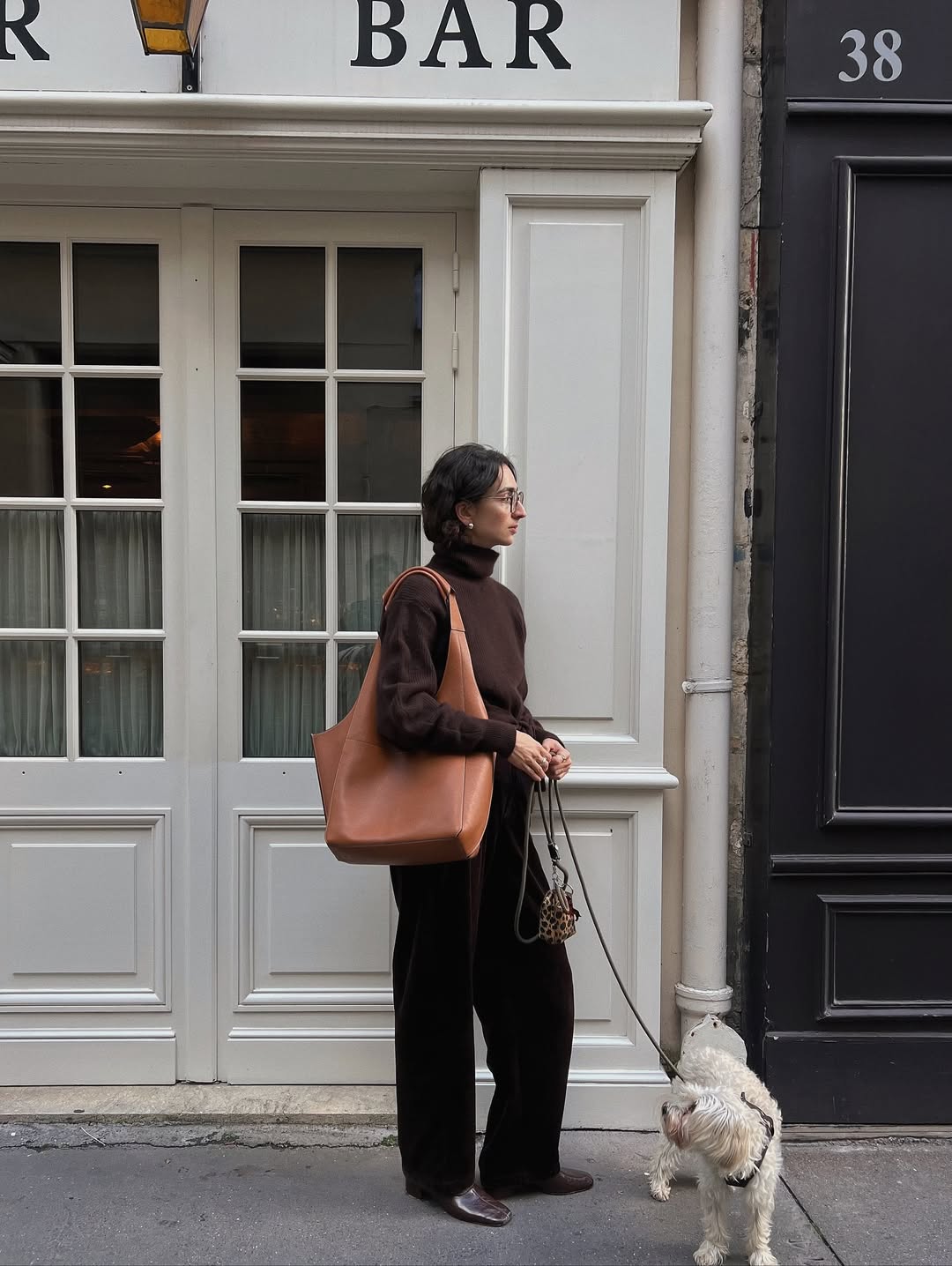 A woman walking her dog wearing black pants, a brown sweater, and leather boots.