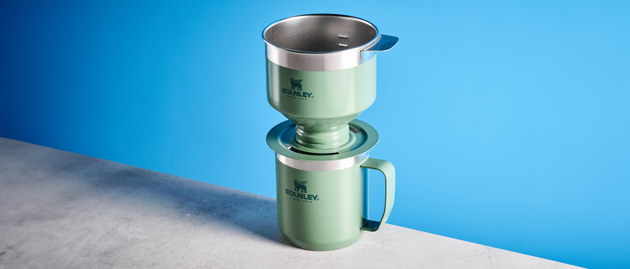 the stanley perfect brew pour over coffee maker in green, photographed with its companion travel mug and with the metal built in filter