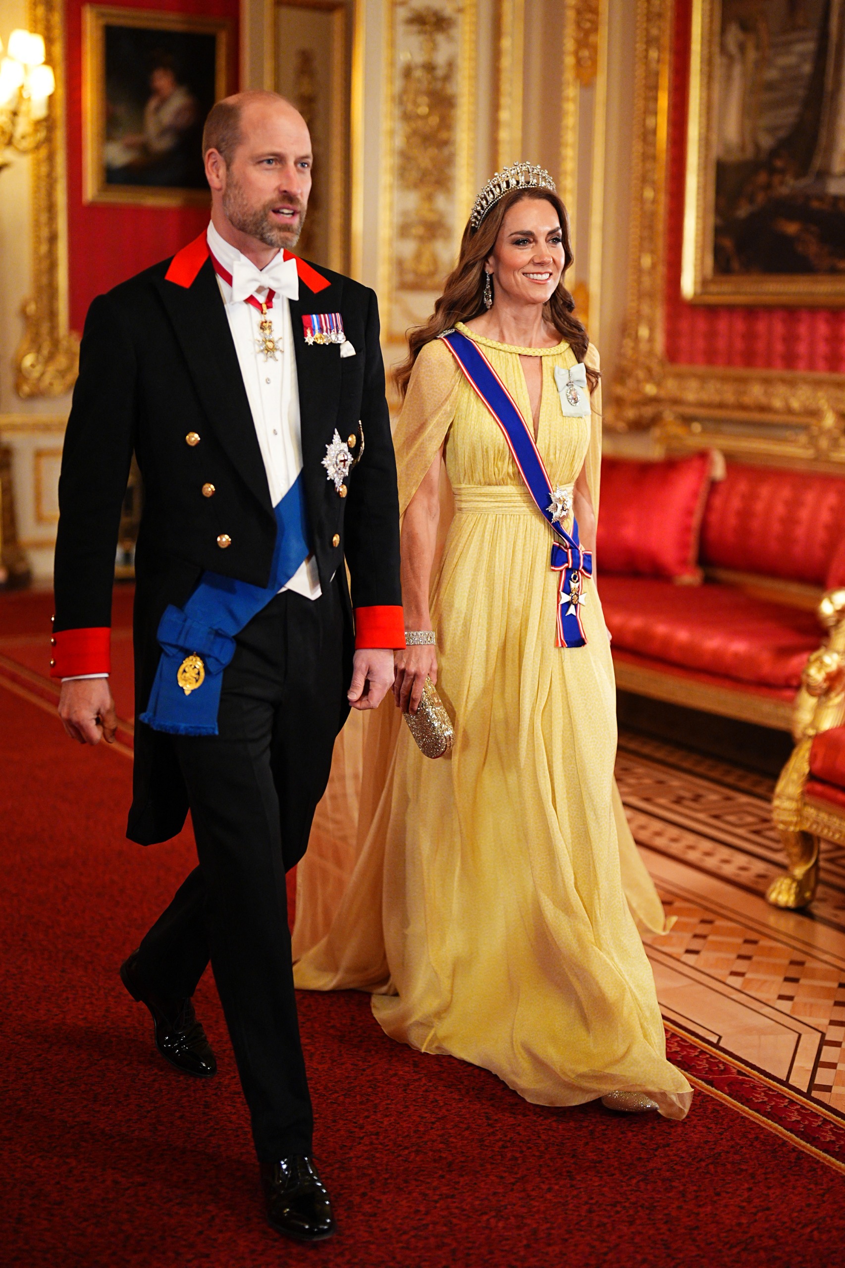 Princess Kate wearing a tiara and yellow gown walking with Prince William at the Omani state banquet