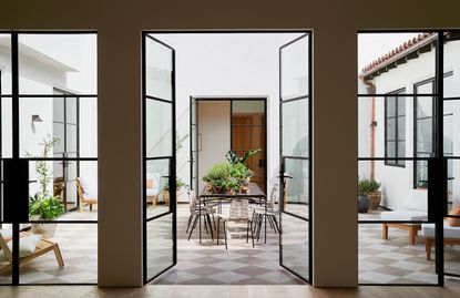 central courtyard with dining table full of plants and white chairs and steel windows through open patio doors