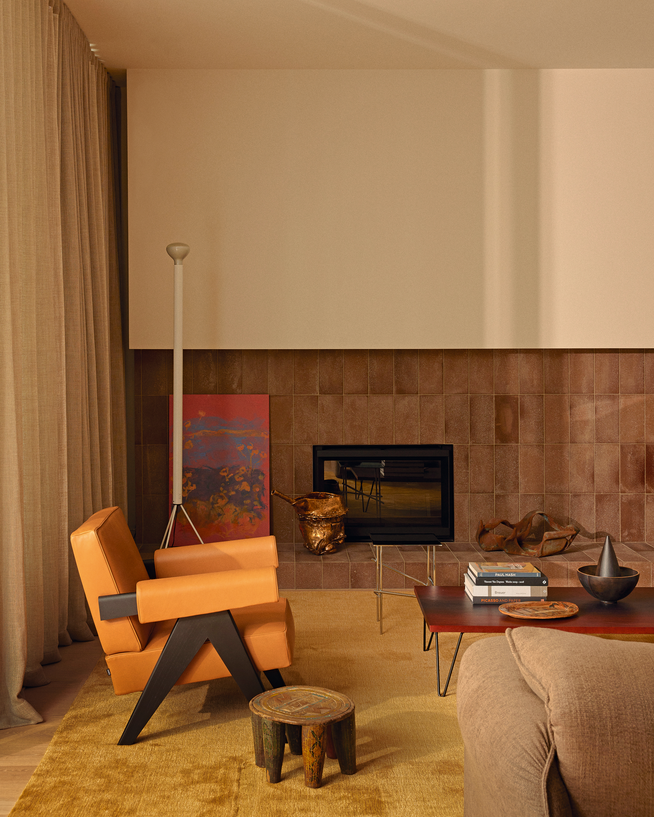 Living area with fireplace set in a half-terracotta tiled wall with an orange armchair and red coffee table