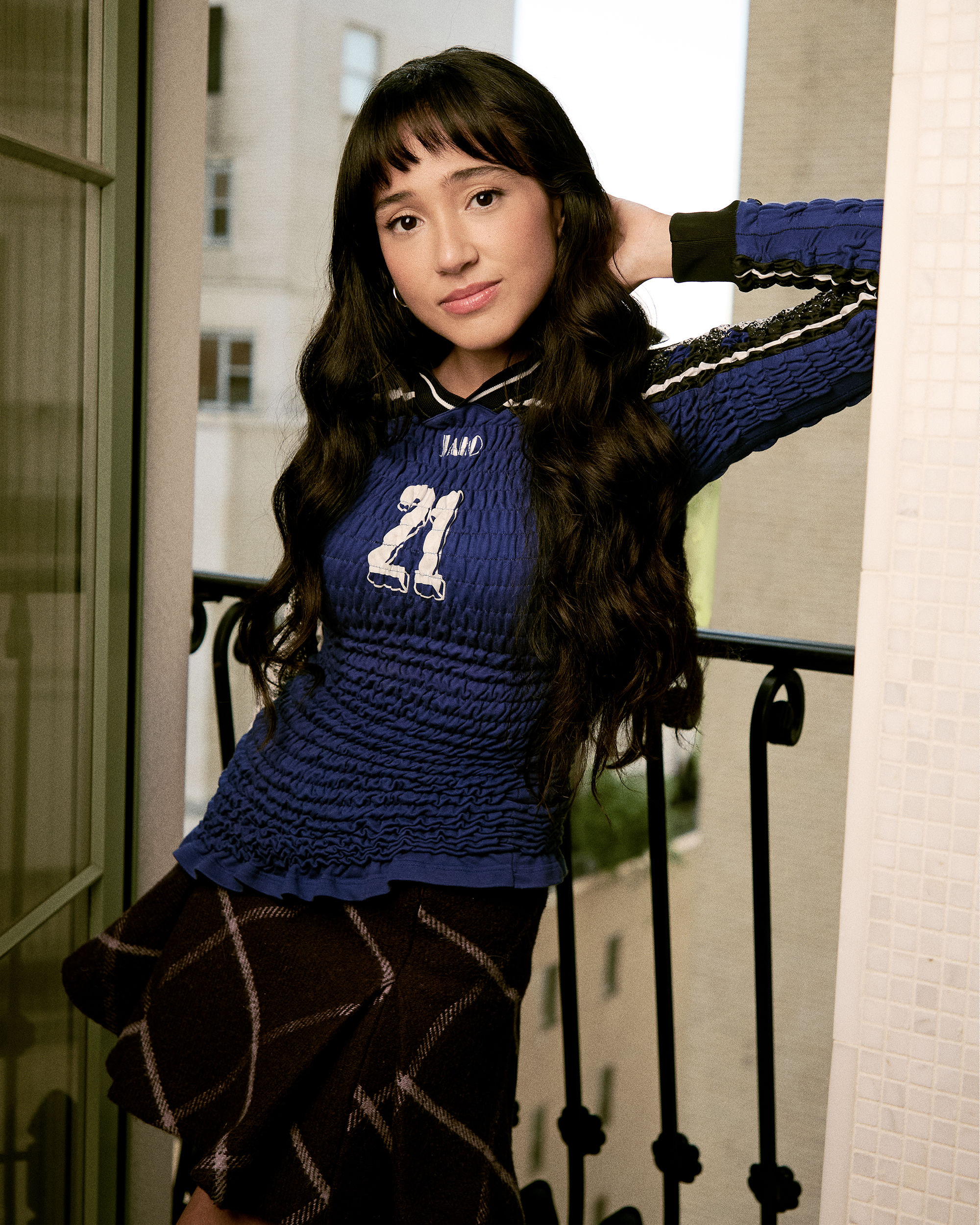 A atriz Wally Baram, que compensa demais, posa para um retrato no Plaza Hotel, em Nova York. Ela veste uma camisa azul de manga comprida com o número 21 na frente, uma minissaia xadrez roxa e botas de couro pretas.
