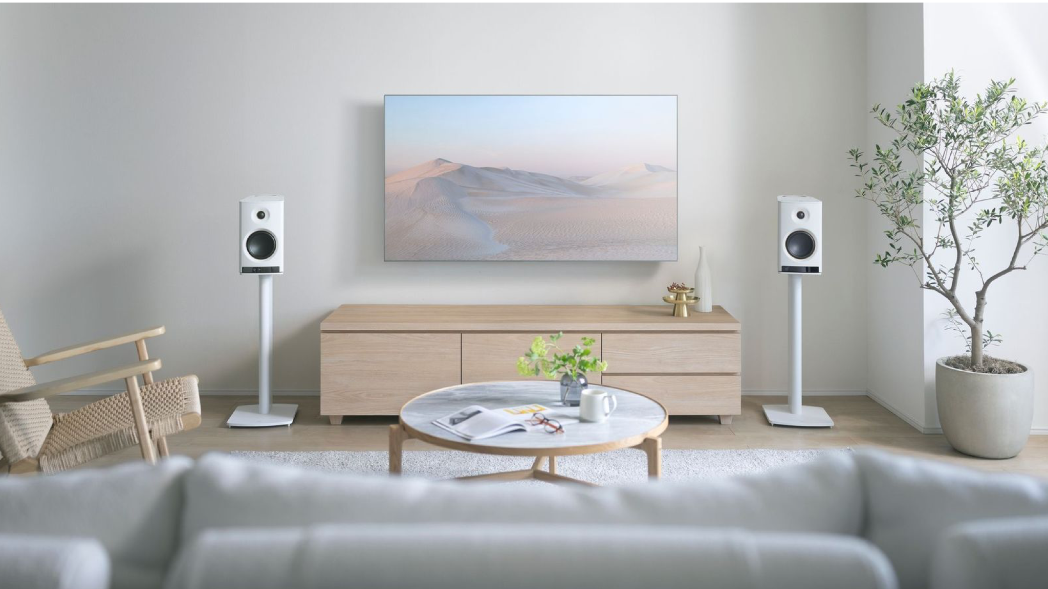 Yamaha NX-70A speakers in white in a neutrally decorated, brightly lit room. They are on stands on either side of a wall mounted television.