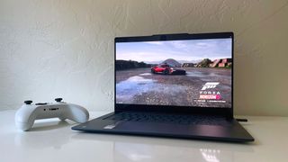 The Lenovo Yoga Slim 7x running Forza Horizon 5 on a white desk next to a white game controller