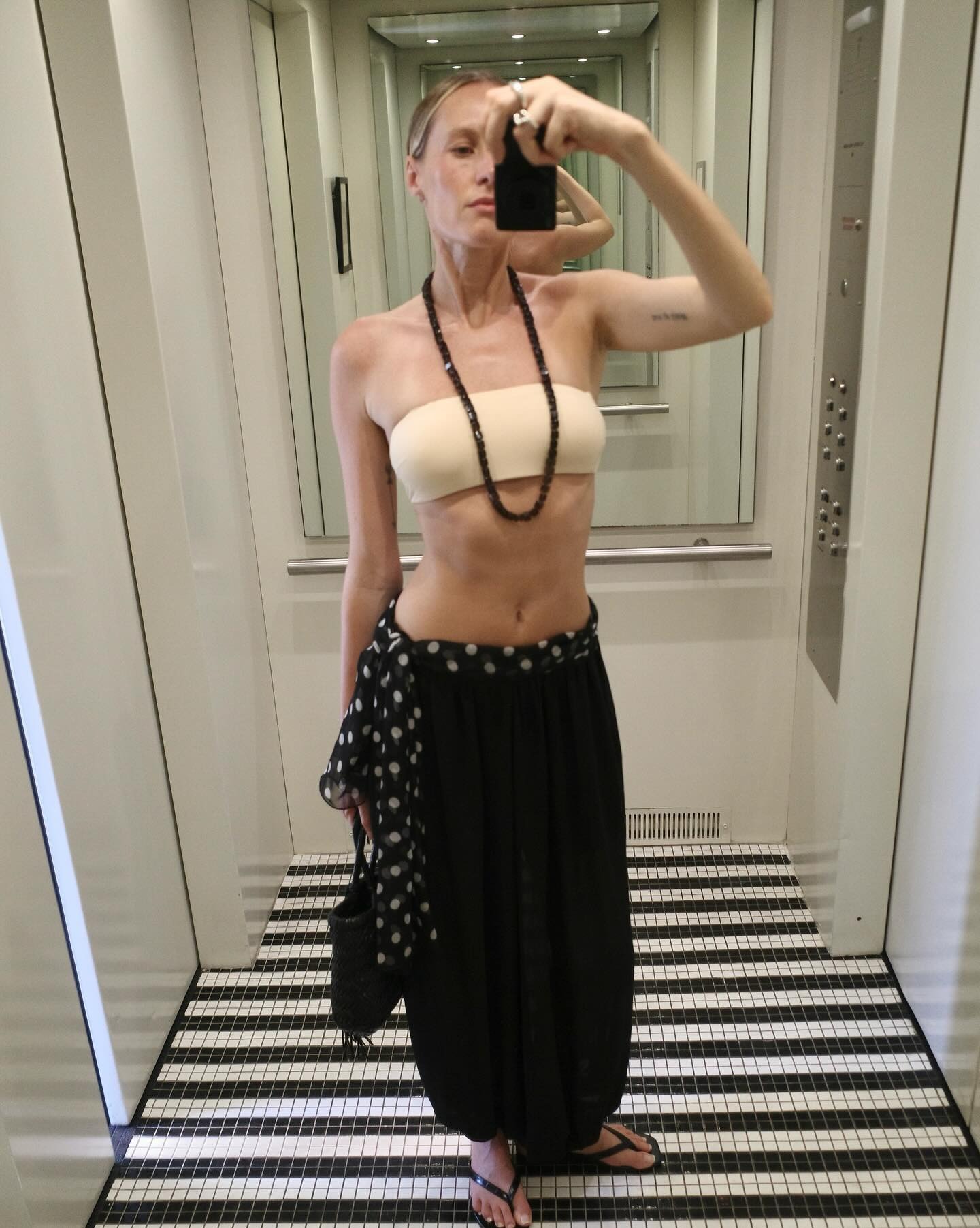 Elly McGaw wearing a strapless tan bralette with a beaded necklace and genie pants.