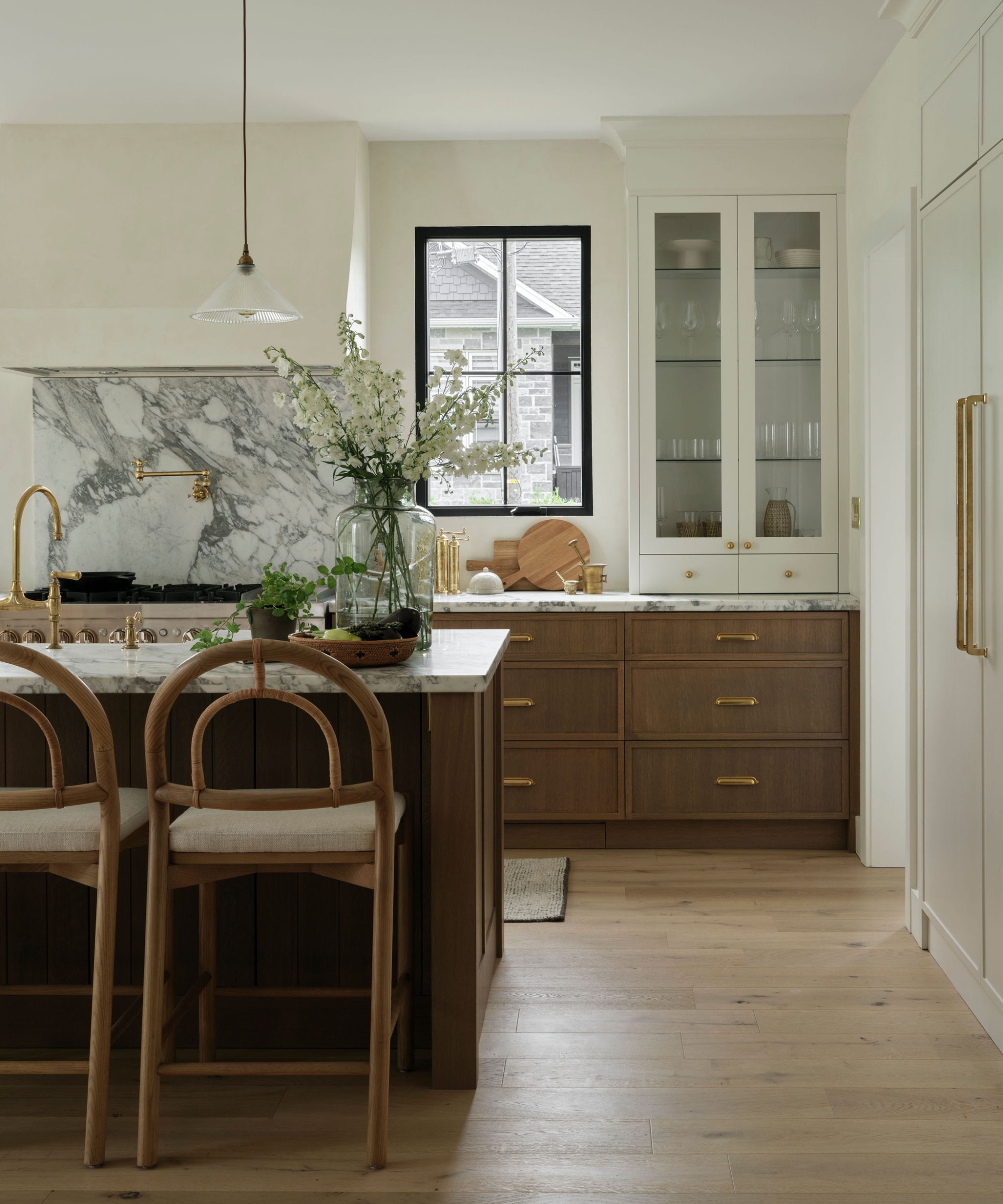A neutral kitchen with wooden cabinets, white walls, and a marble backsplash behind the cooktop