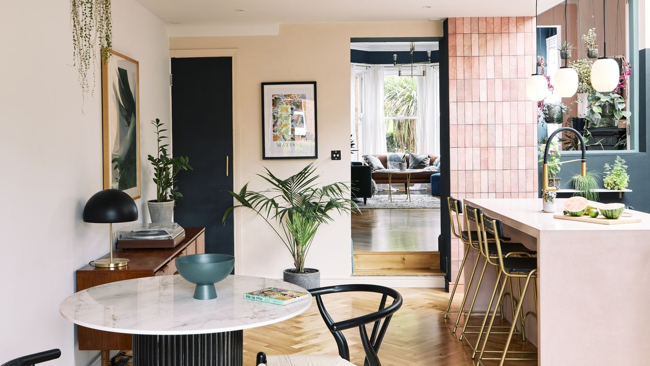 Kitchen-diner with pink tiled wall, peach painted walls, pink island and marble and black dining set