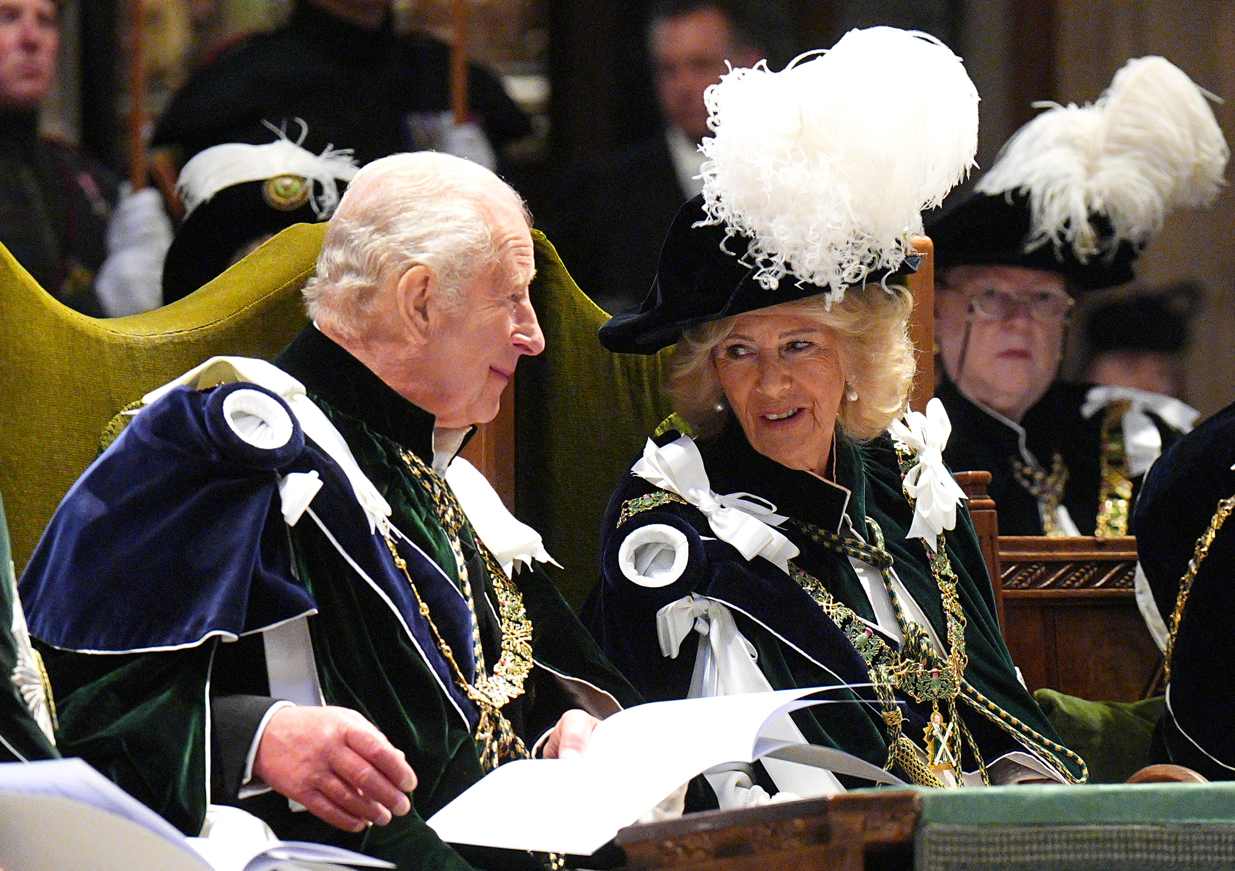King Charles and Queen Camilla wearing velvet robes and smiling at each other