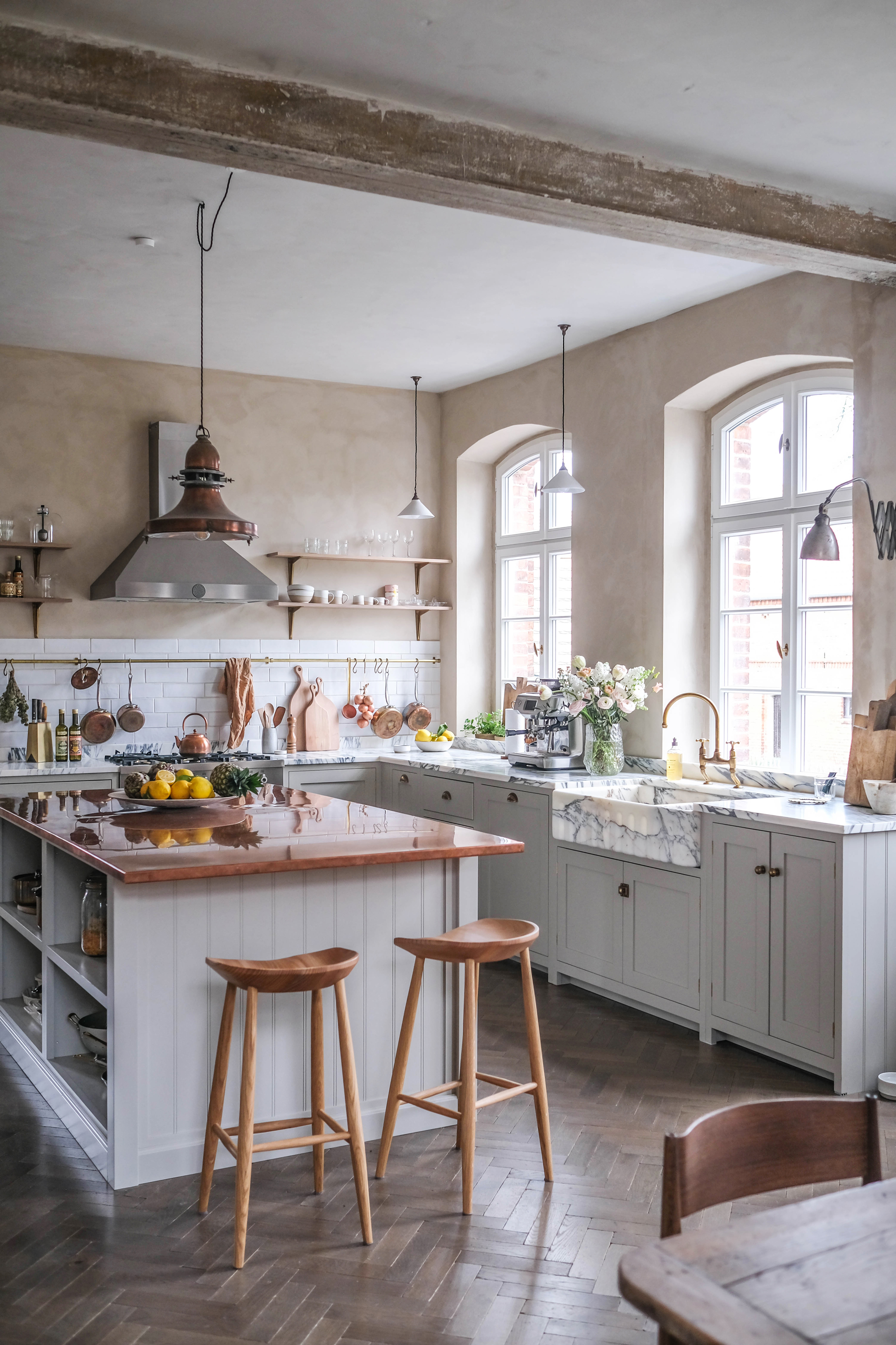 white kitchen cabinetry, white kitchen island with copper top, open shelving, plaster coloured walls, marble countertops, parquet flooring