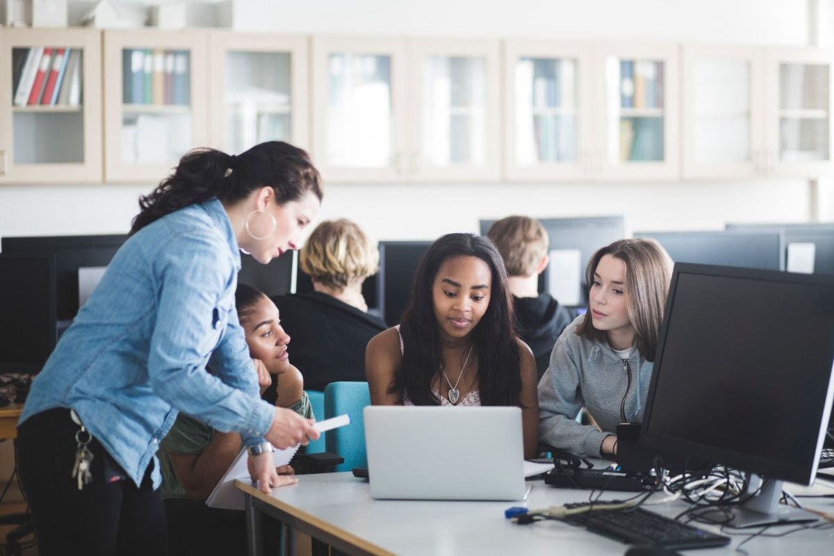 Teacher assisting female students using laptop in computer lab at high school